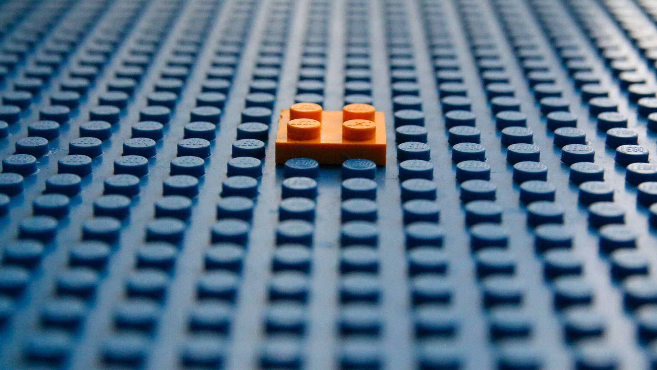 a small orange lego brick on a larger panel of blue lego brick