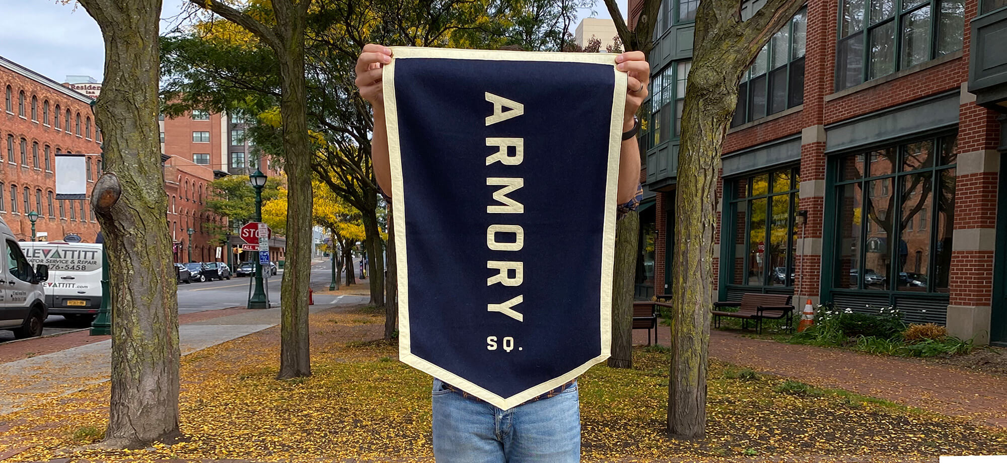 a large blue flag that says “Armory Sq.” being held up outdoors in the fall