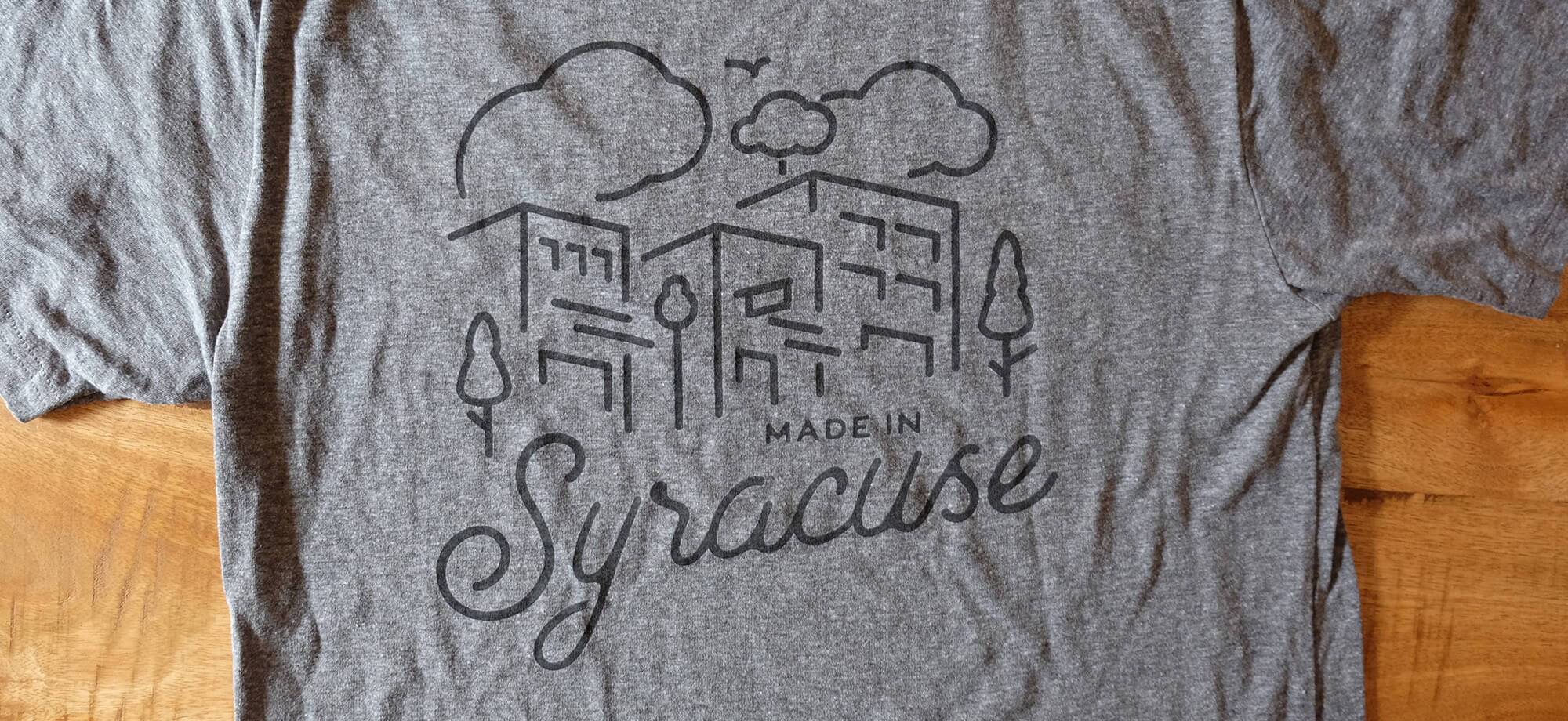 a gray tee on a wood table. the tee reads “Made in Syracuse”
