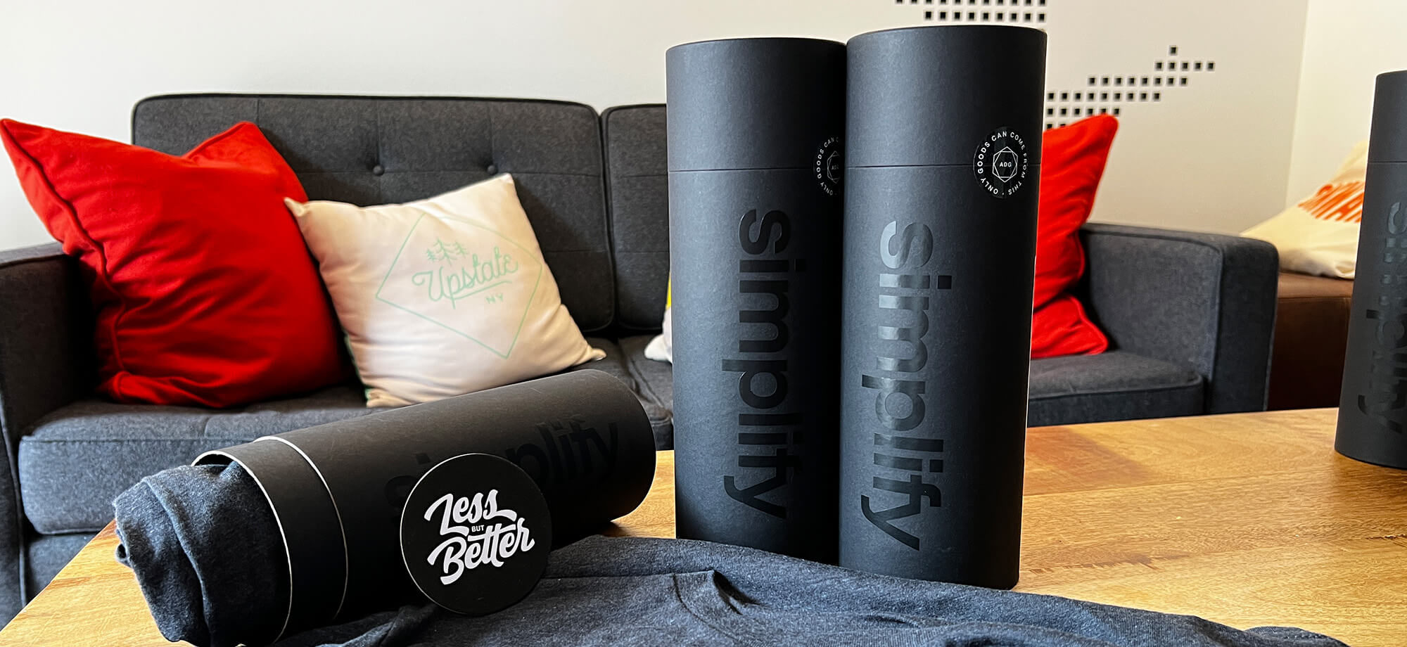 the contents of our simplify kit (tee, tube, coaster that says “Less but Better” on a coffee table in our studio