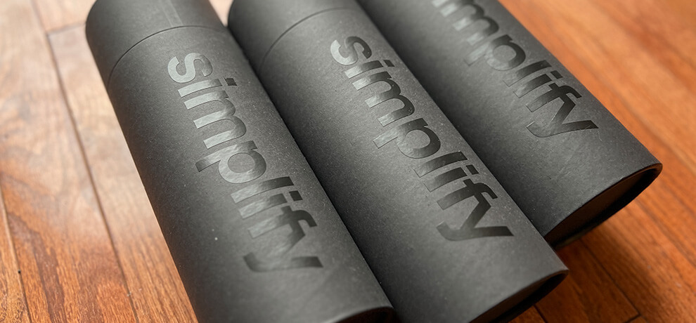 three black paper tubes that say “simplify” on a hardwood floor