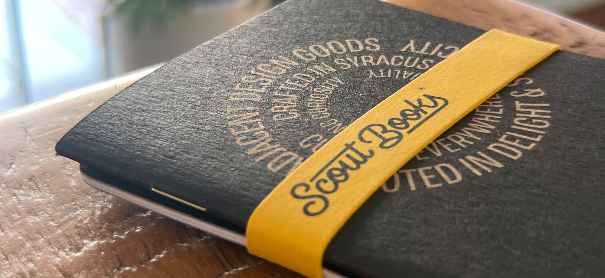 a closeup of a black notebook with a yellow rubber band on it that says Scoutbooks
