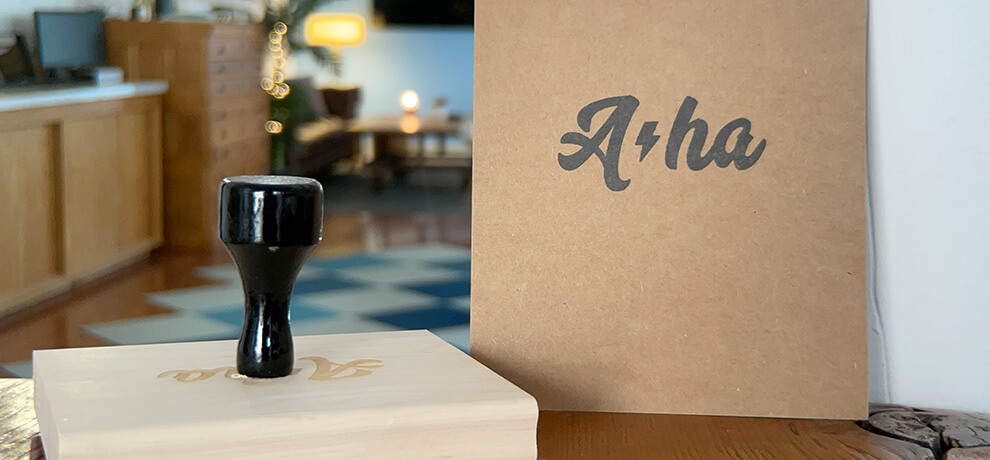 a kraft postcard stamped “A-ha”, standing next to the stamp itself