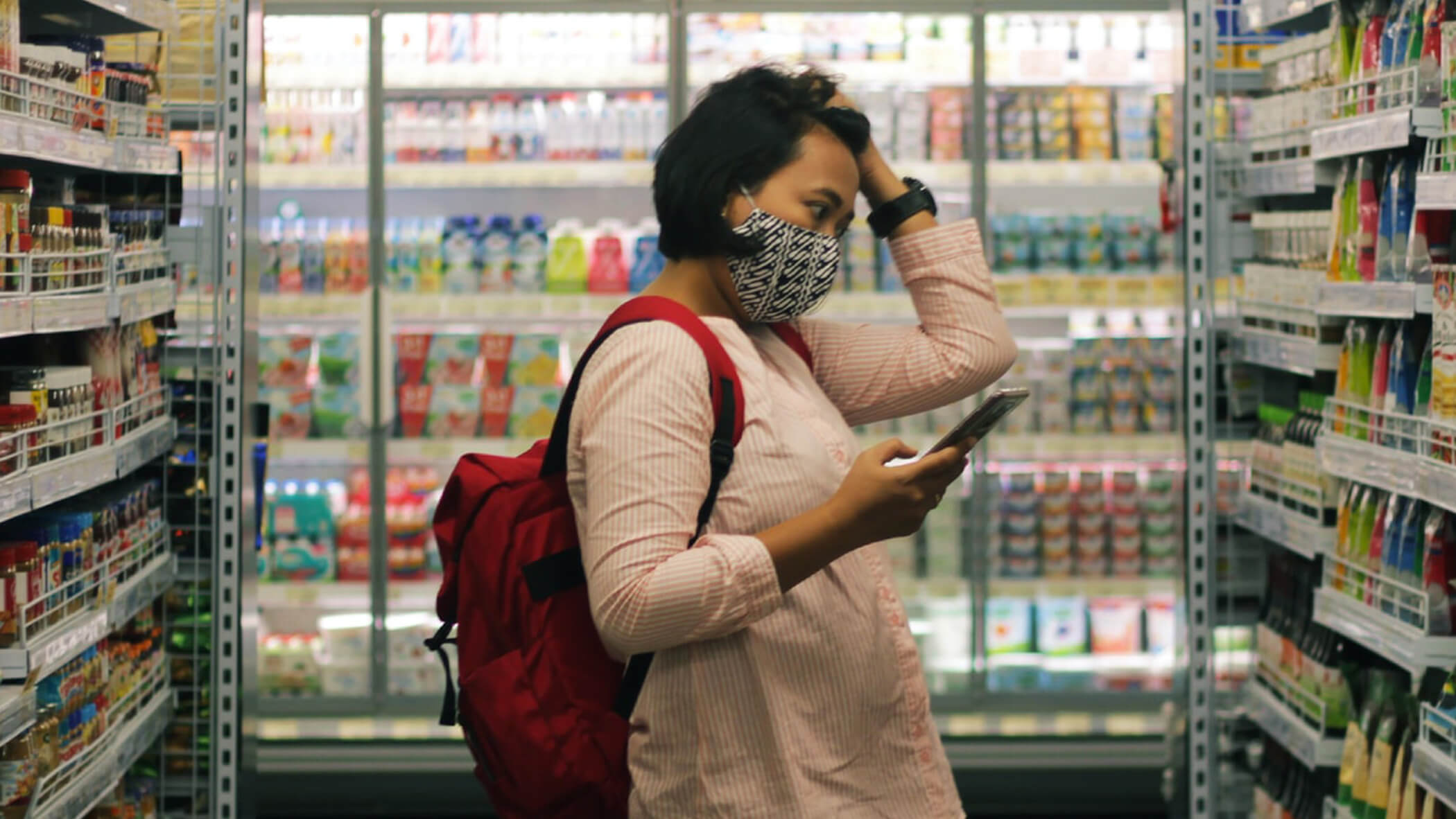 a woman in a grocery store, looking for an item and holding a phone