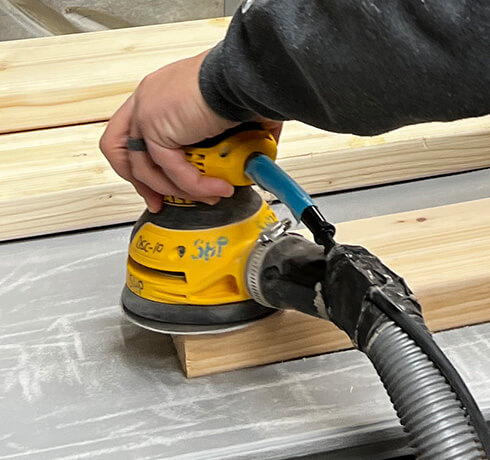 a hand using an electric sander on a plank of wood